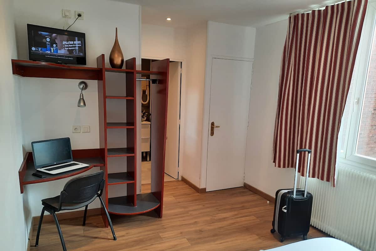 Une chambre d’hôtel équipée d’un bureau, d’un ordinateur portable, d’une chaise, d’une armoire, d’une valise et d’un téléviseur.