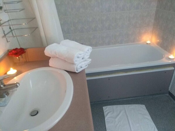 A bathroom with a sink, a bathtub, and a mirror. There are two candles on the floor.