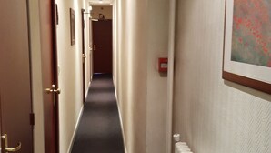 A hotel hallway with doors on both sides, a radiator on the right, and a framed picture on the wall.