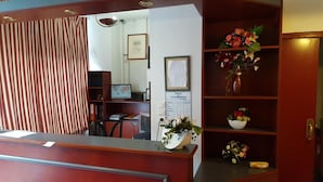 A reception area with a wooden reception desk, a framed price list on the wall, and shelves with decorative flowers and a bowl.