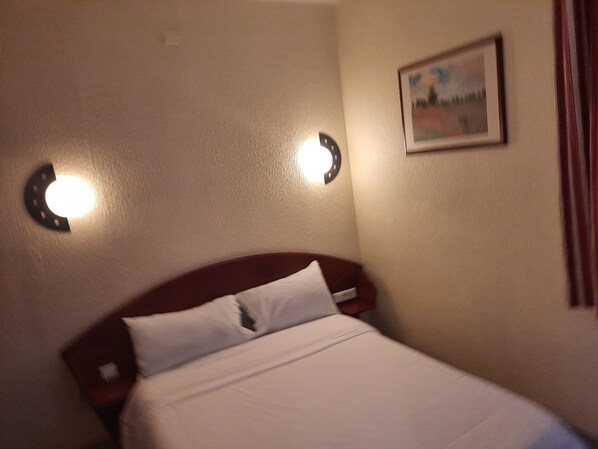 A hotel room with a bed, a headboard, and two wall-mounted lights. - Hôtel le Clémenceau (Valenciennes)