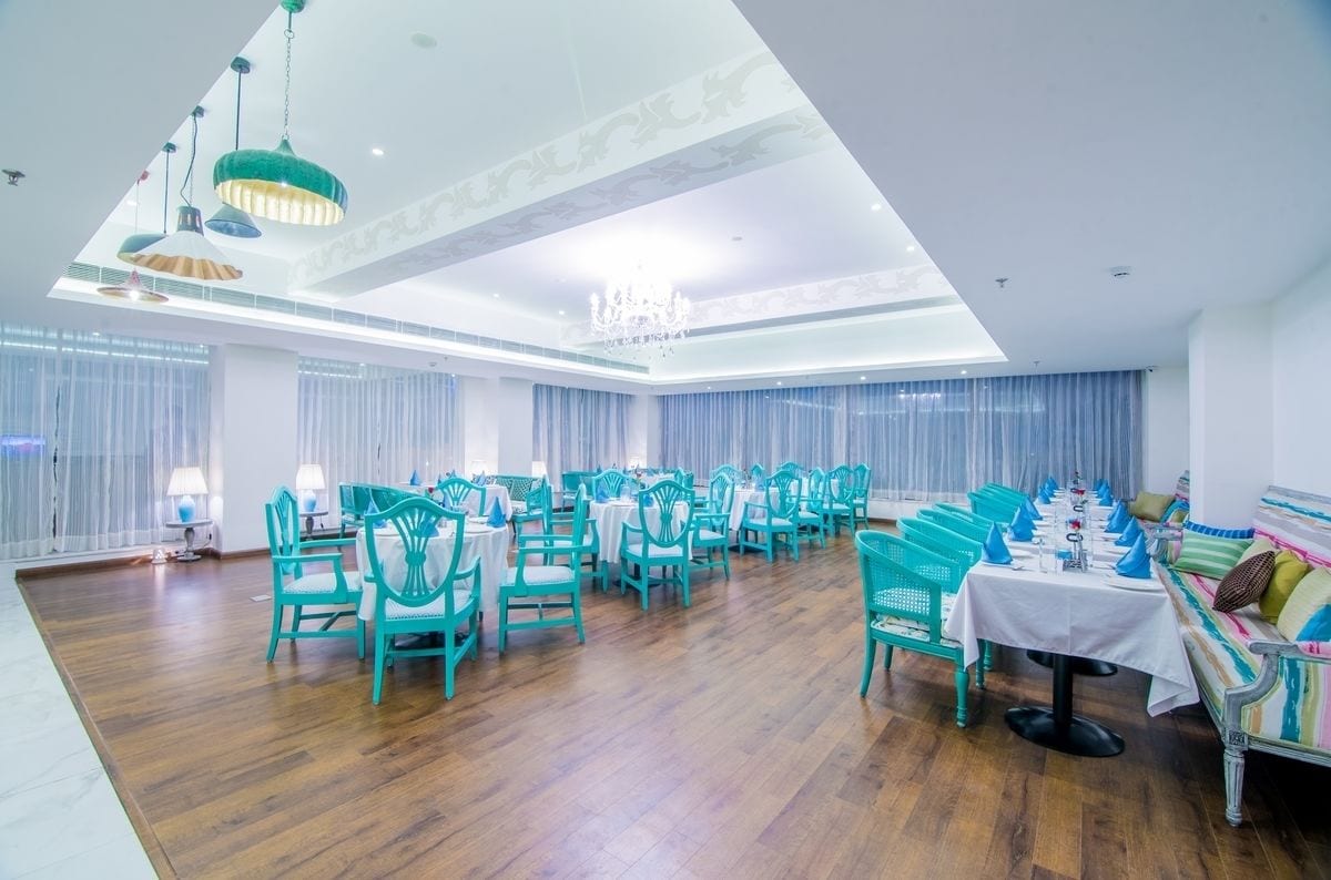 Un comedor amplio con sillas y mesas color turquesa, una araña y un techo alto con tragaluces.