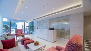 A modern lobby with a reception desk, seating area, and large windows offering a view of the outdoors.