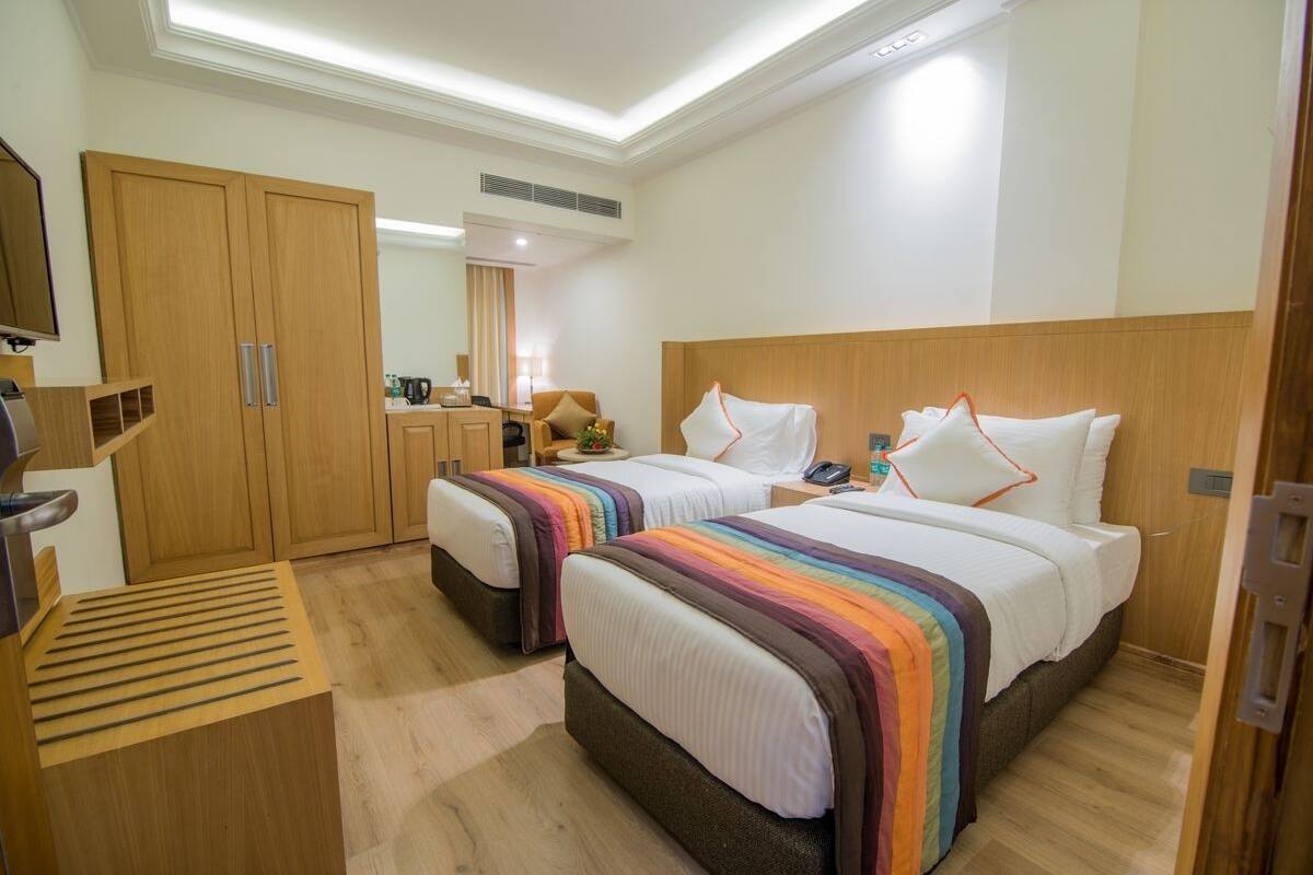 Een hotelkamer met twee bedden, een houten kledingkast, een bureau met lamp en een kleine kitchenette.