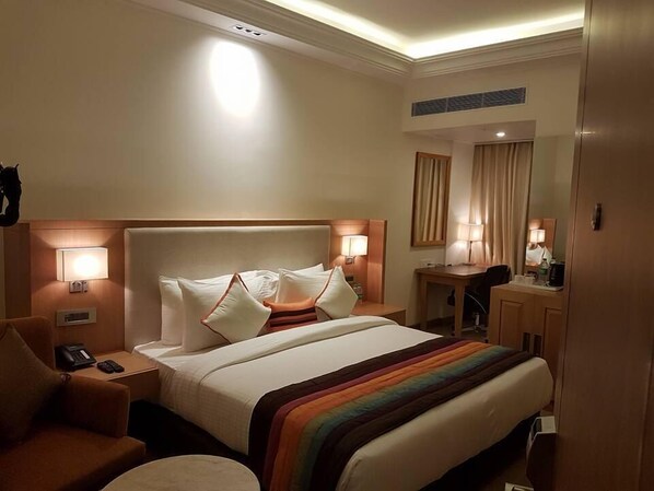 A hotel room with a large bed, two bedside lamps, a desk with a chair, and a mirror.