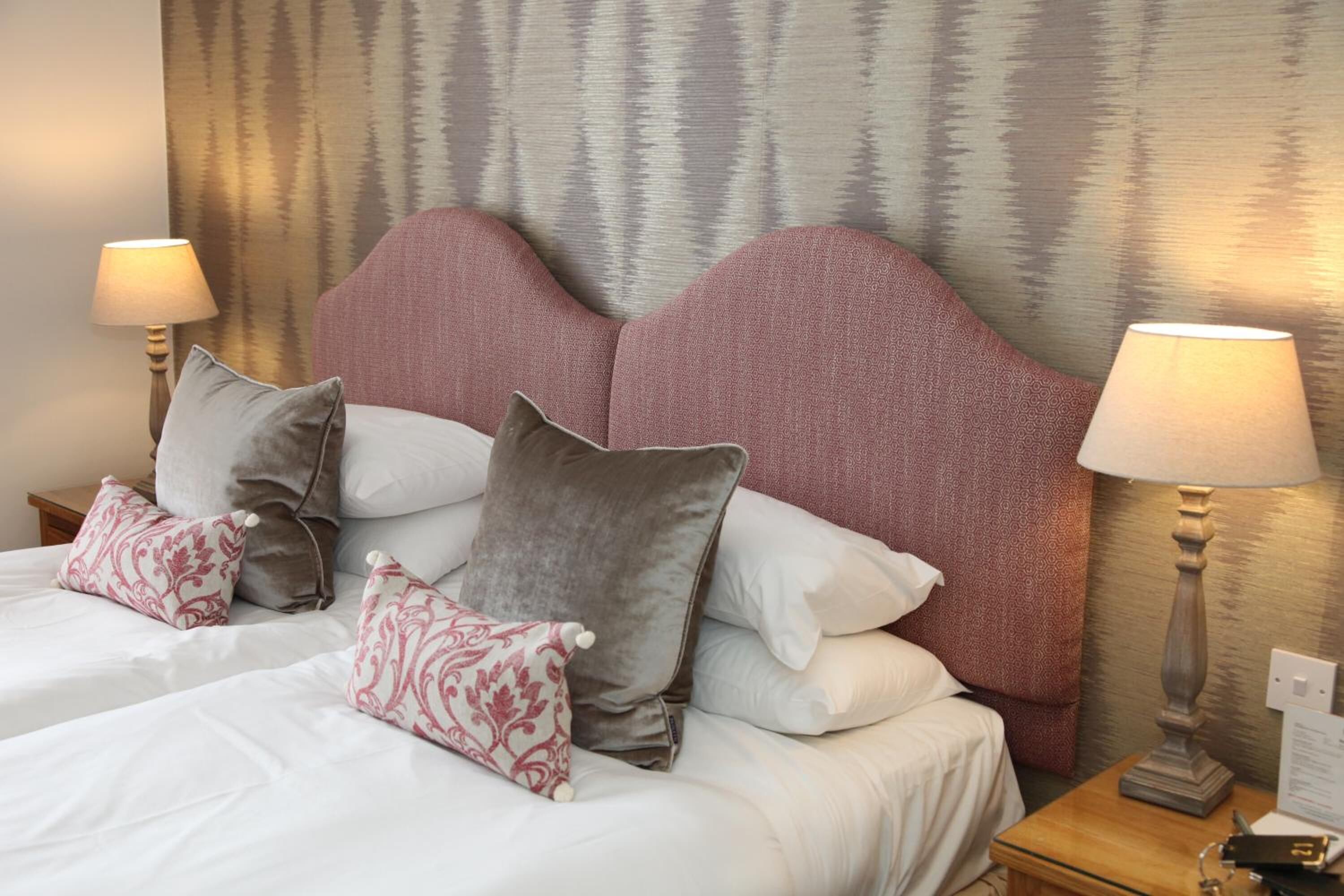 A hotel room with a large bed, multiple pillows, two bedside lamps, and a textured wall behind the bed.