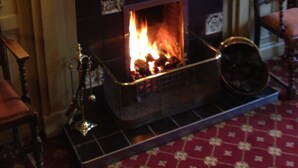 Una chimenea encendida, un espejo encima y dos libros rojos sobre la repisa.