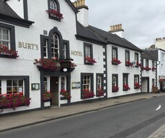 A traditional white building with black trim, labeled "Burt's Hotel," featuring multiple windows with flower boxes and a signboard.