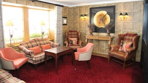 Habitación con alfombra roja, paneles de madera, una obra de arte grande enmarco y varias opciones de asientos, incluyendo un sofá y sillones.