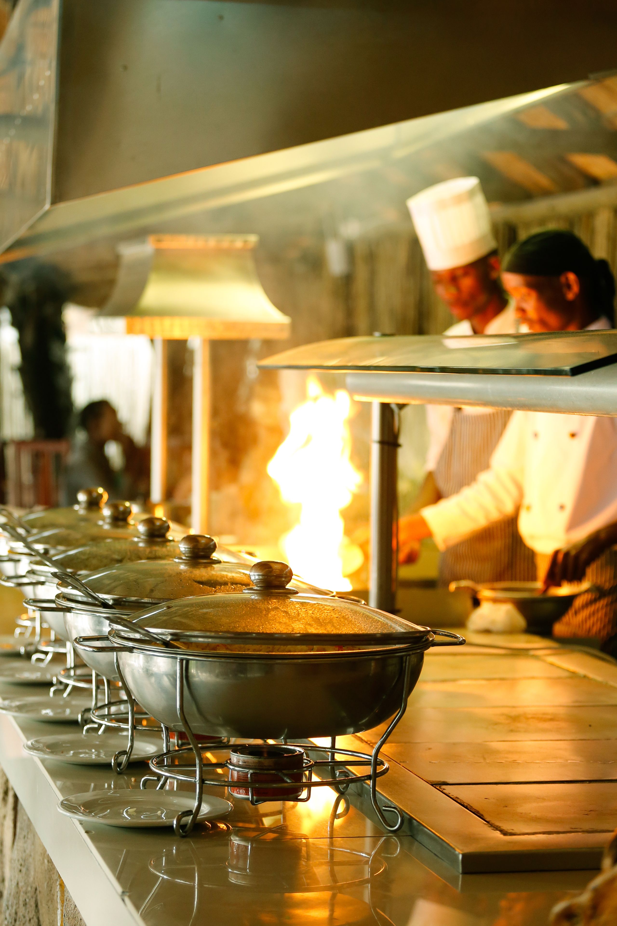 A kitchen with stainless steel pots on a stove, a chef in uniform, and a person in the background.