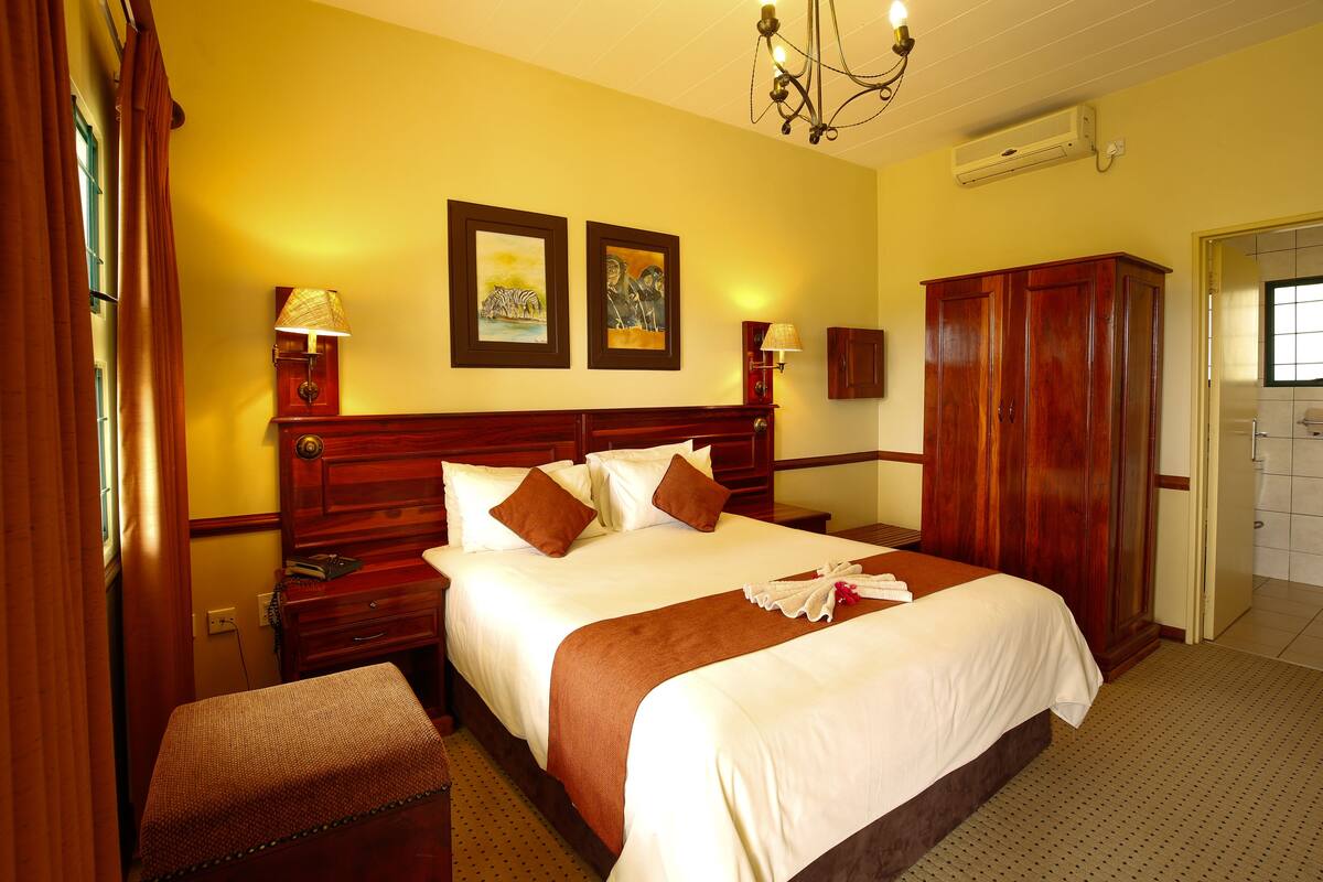 A hotel room with a large bed, wooden headboard, two wall-mounted lamps, a wardrobe, and a small bench.