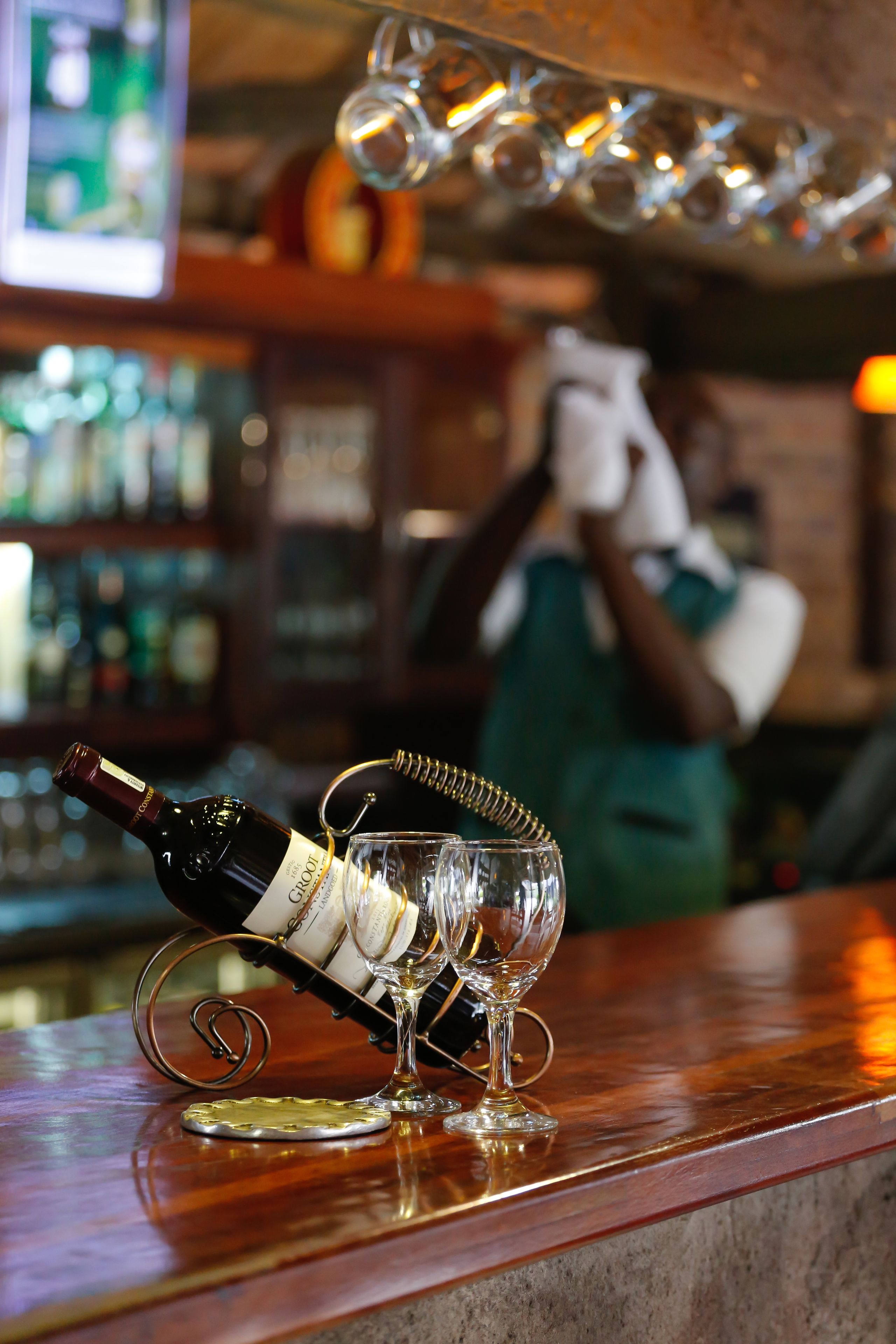 A bottle of wine on a coaster with a glass, and a bar area with shelves in the background.