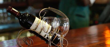 A bottle of wine on a coaster with a glass, and a bar area with shelves in the background.