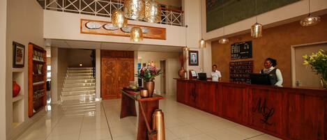 Un vestíbulo de hotel con una recepción, una escalera y un cuadro grande en la pared.