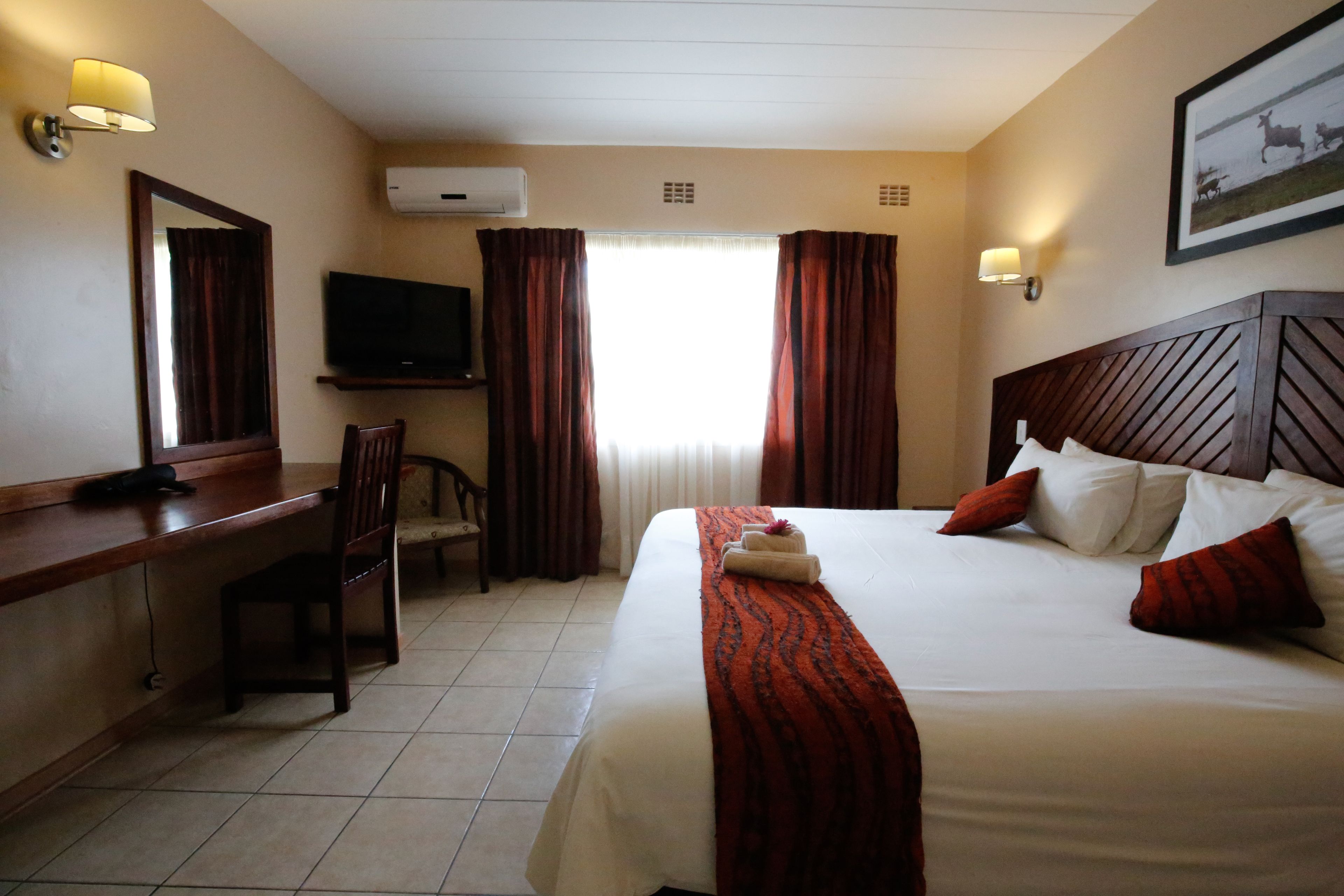 Una habitación de hotel con cama, escritorio, silla, televisor y ventana con cortinas.