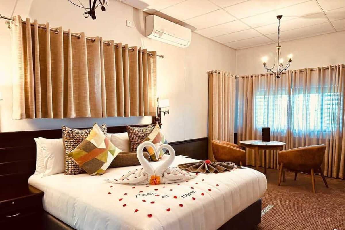 A hotel room with a large bed, a small table, a chair, and curtains.