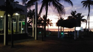Una propiedad frente al mar con una estructura de cristal, palmeras y vistas al atardecer.