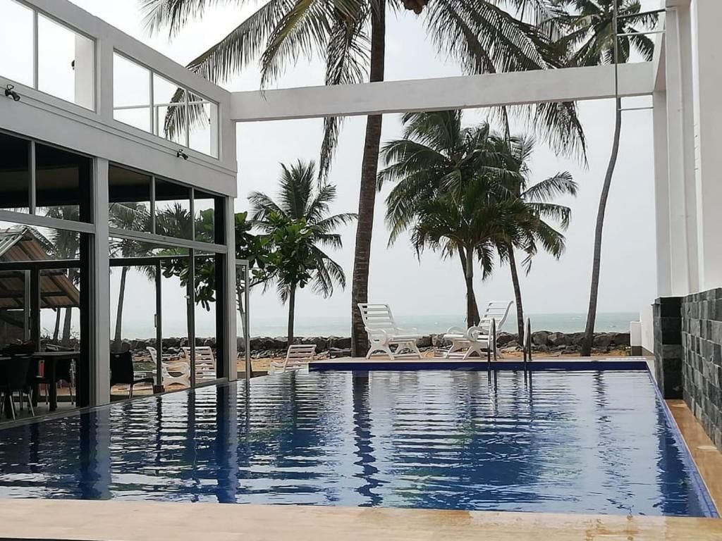 Piscina con sillones de descanso, palmeras y vista a la playa.