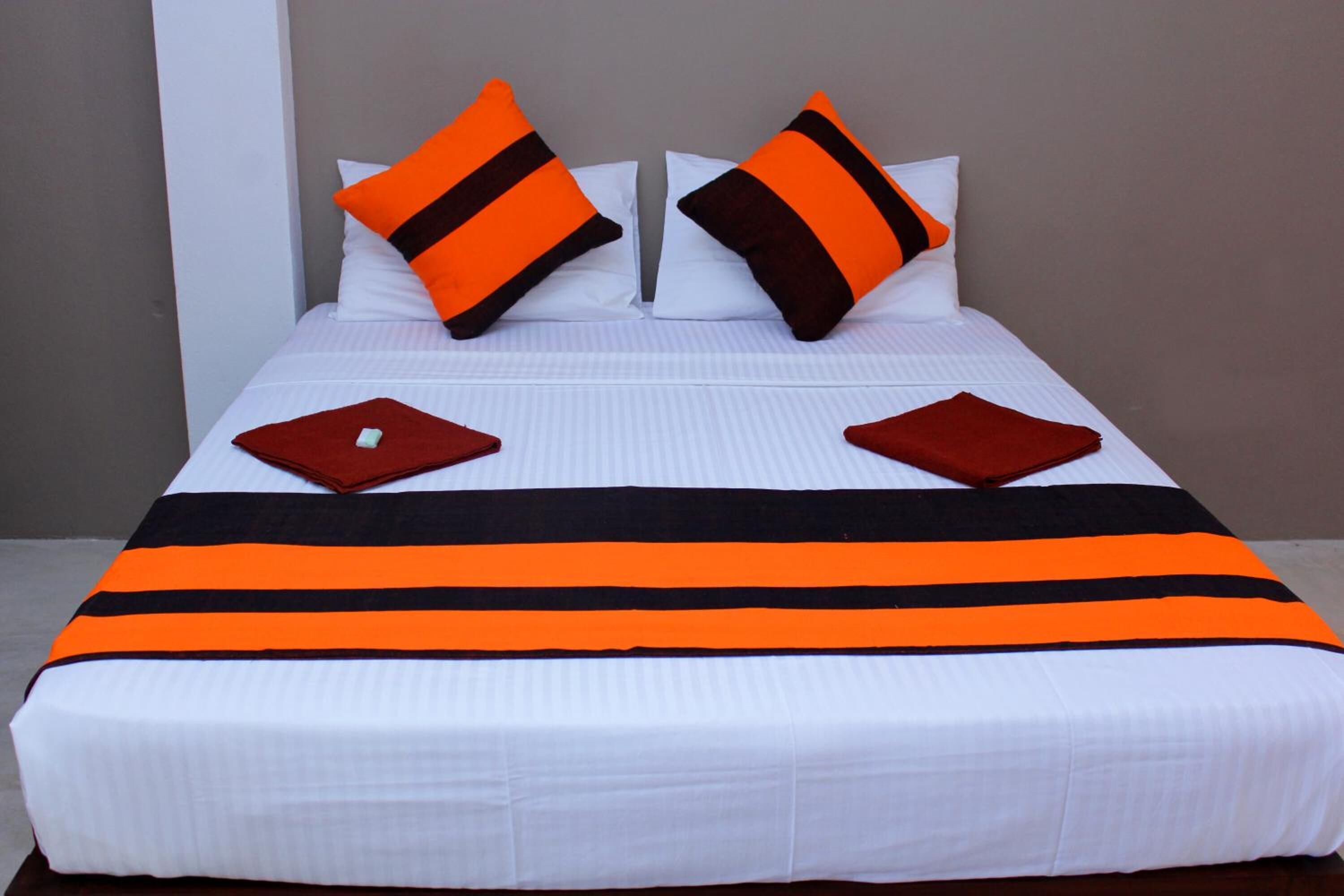 A neatly made bed with white bedding, two orange pillows, and a black and orange striped bedspread.