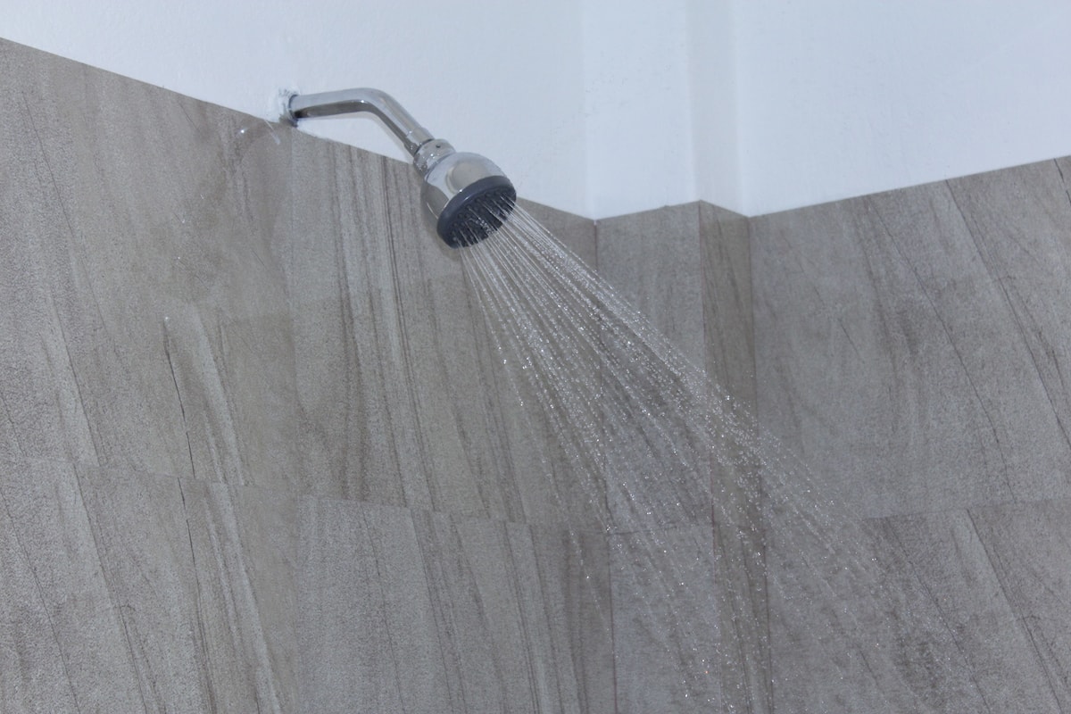 Een douchekop met water dat langs een wand met een structuur stroomt.