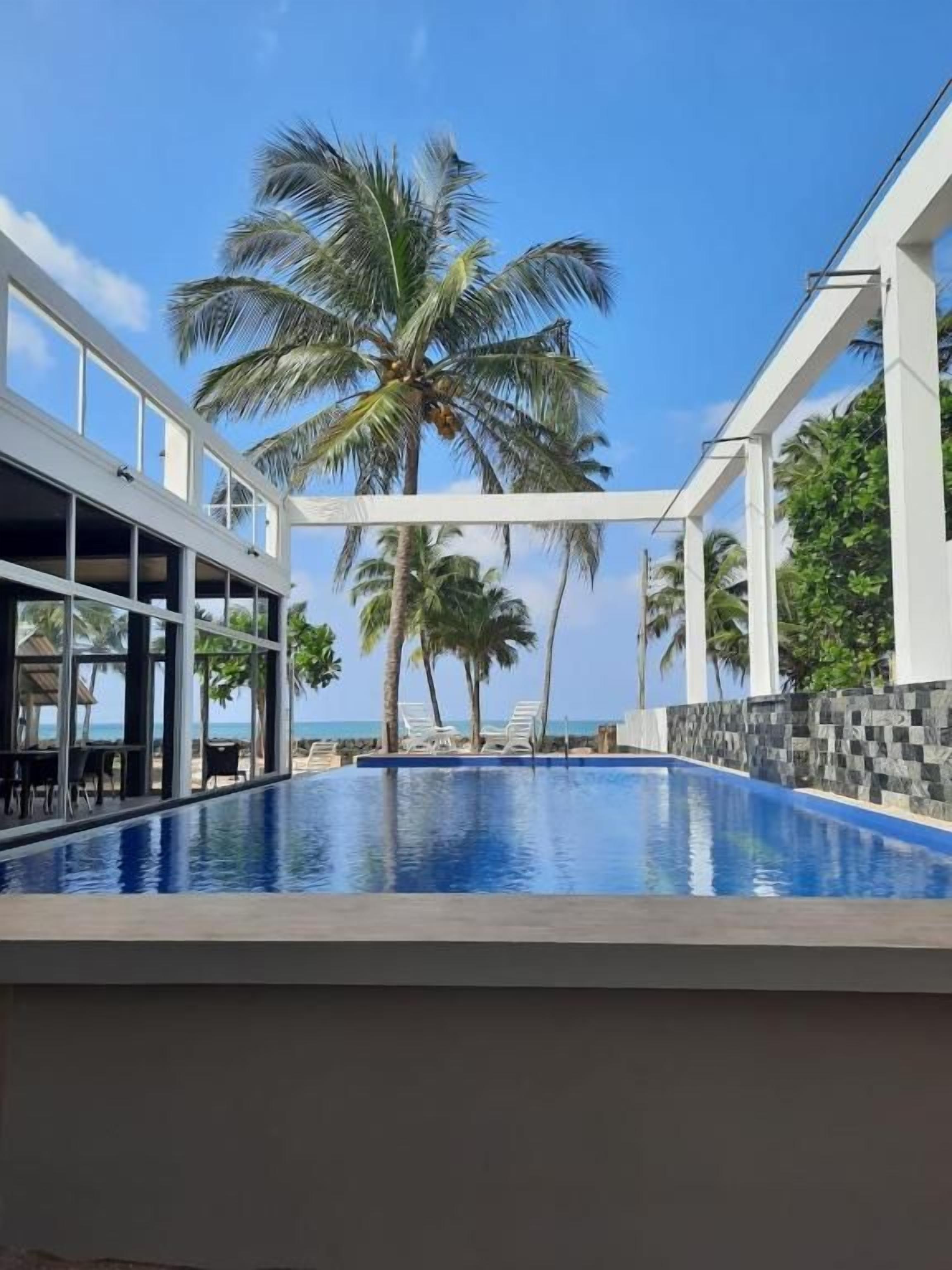 A pool area with a view of the ocean, palm trees, and a modern building structure.
