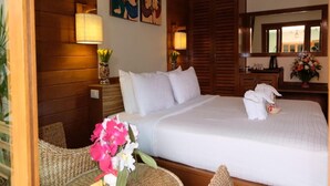 A hotel room with a large bed, wooden headboard, two wall-mounted lamps, a wooden wardrobe, and a mirror above the bed. - Vieng Mantra (Chiang Mai)