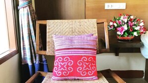 A wooden chair with a woven seat and backrest, a red cushion with white patterns, and a small table with a vase of flowers. - Vieng Mantra (Chiang Mai)