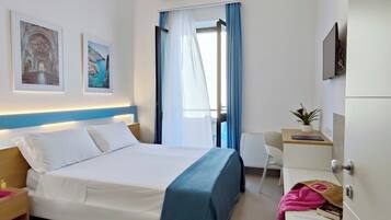 Ein Hotelzimmer mit Bett, Schreibtisch, Stuhl, Fernseher und einem Fenster mit Vorhängen.