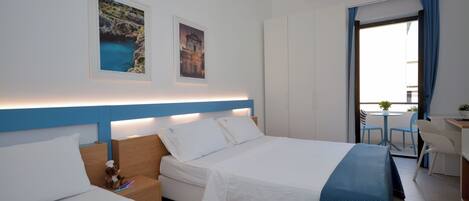 Een hotelkamer met twee bedden, een bureau en een balkon met uitzicht op zee.