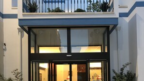 A hotel entrance with a glass door, a reception desk inside, and outdoor seating with potted plants. - Hotel Miramare (Otranto)