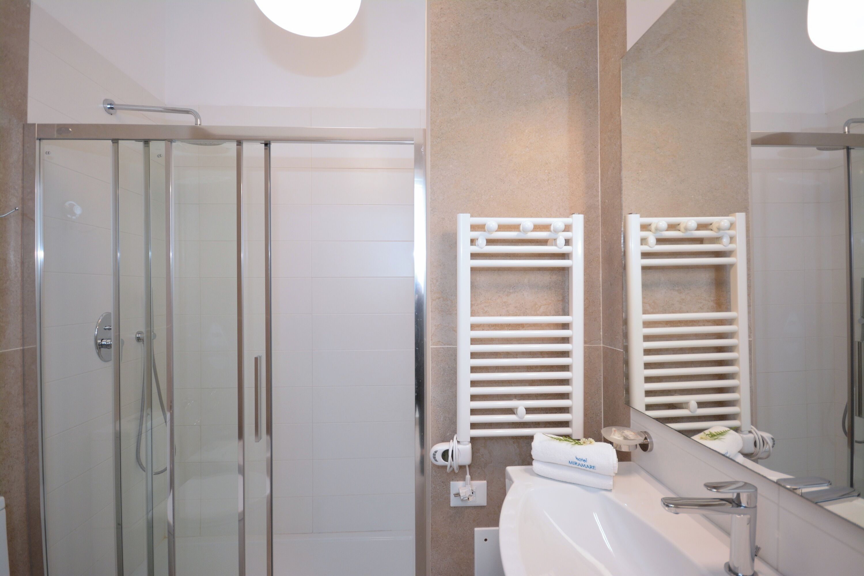 A modern bathroom with a glass-enclosed shower, a white sink, and a large mirror.