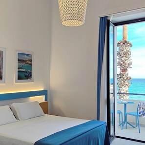 Un cuarto de hotel con cama, ventana grande y vista al mar.