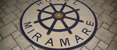 Un mosaico circular con las palabras "HOTEL MIRAMARE" y un diseño de timón de barco.