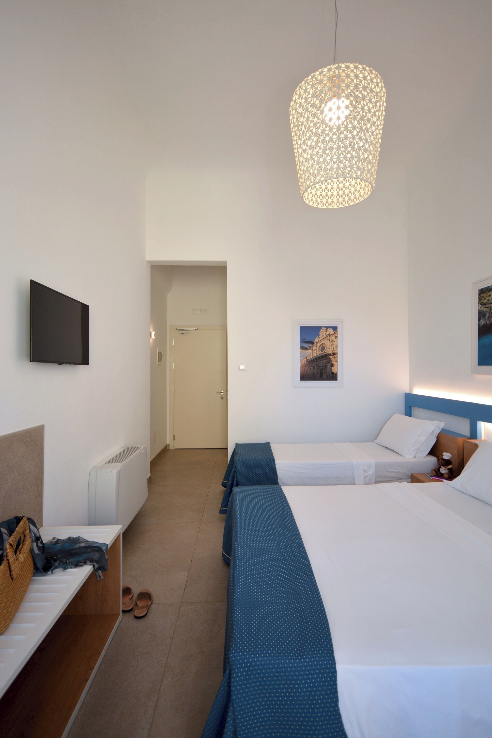 A hotel room with two beds, a television on the wall, a door, and a hallway leading to another room.
