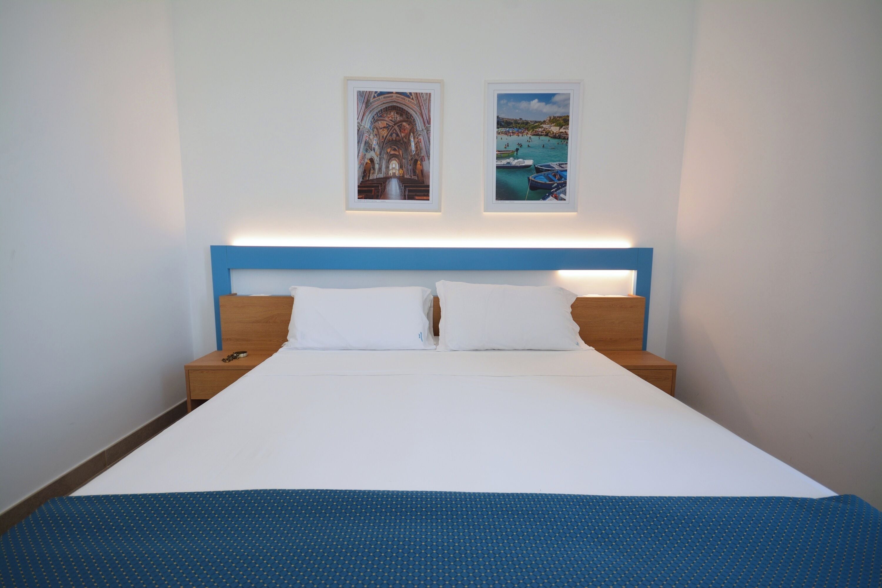 Una cama bien hecha con cabecera azul, ropa de cama blanca y dos cuadros en la pared.