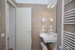 Un baño moderno con un lavamanos blanco, espejo y perchero. Hay dos secadores de pelo montados en la pared.