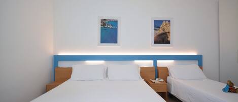 Una habitación de hotel con una cama grande, dos camas más pequeñas, una mesita de noche con un teléfono y dos cuadros enmarcados en la pared.