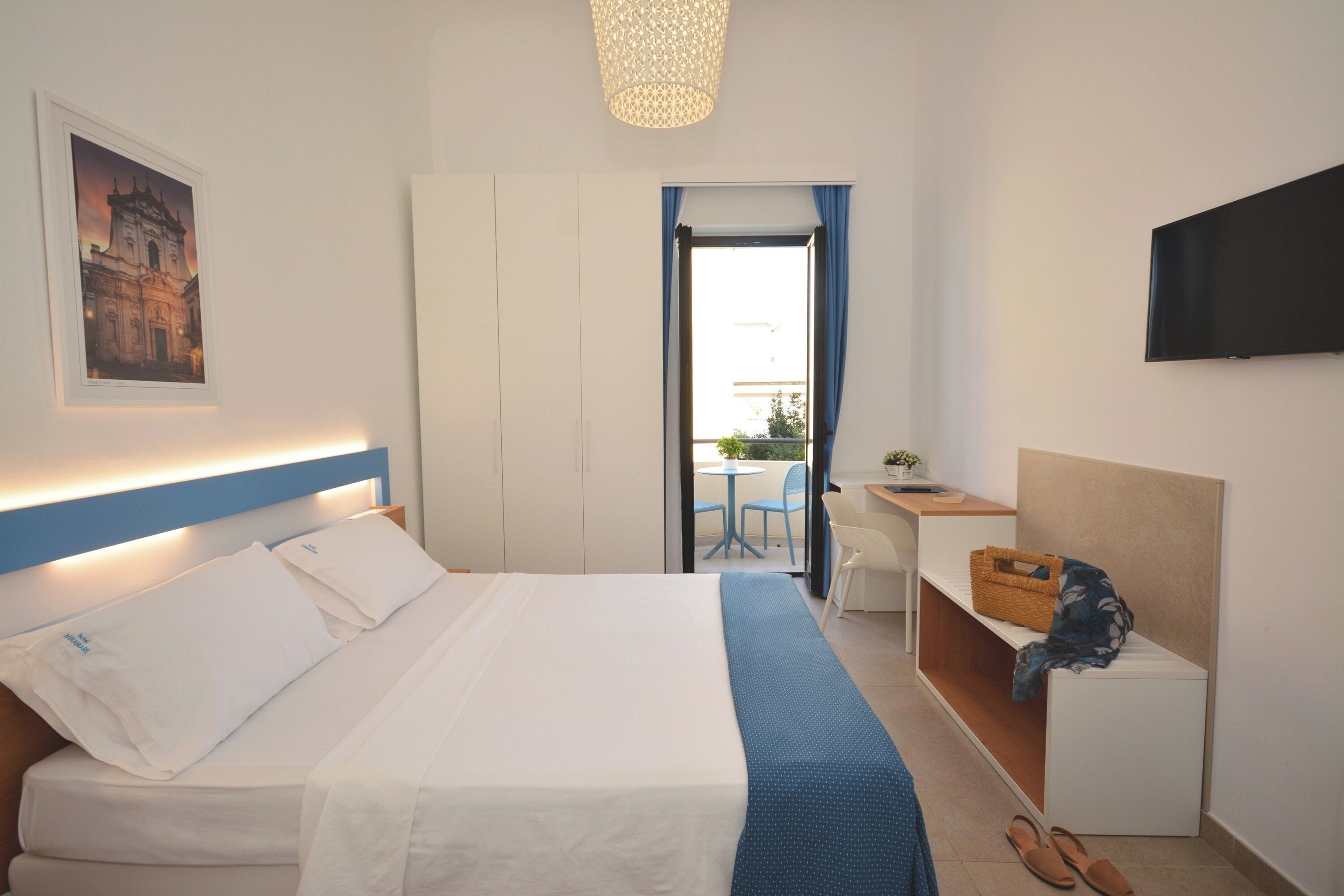 Habitación de hotel con cama, escritorio, silla, televisor y ventana con cortinas.