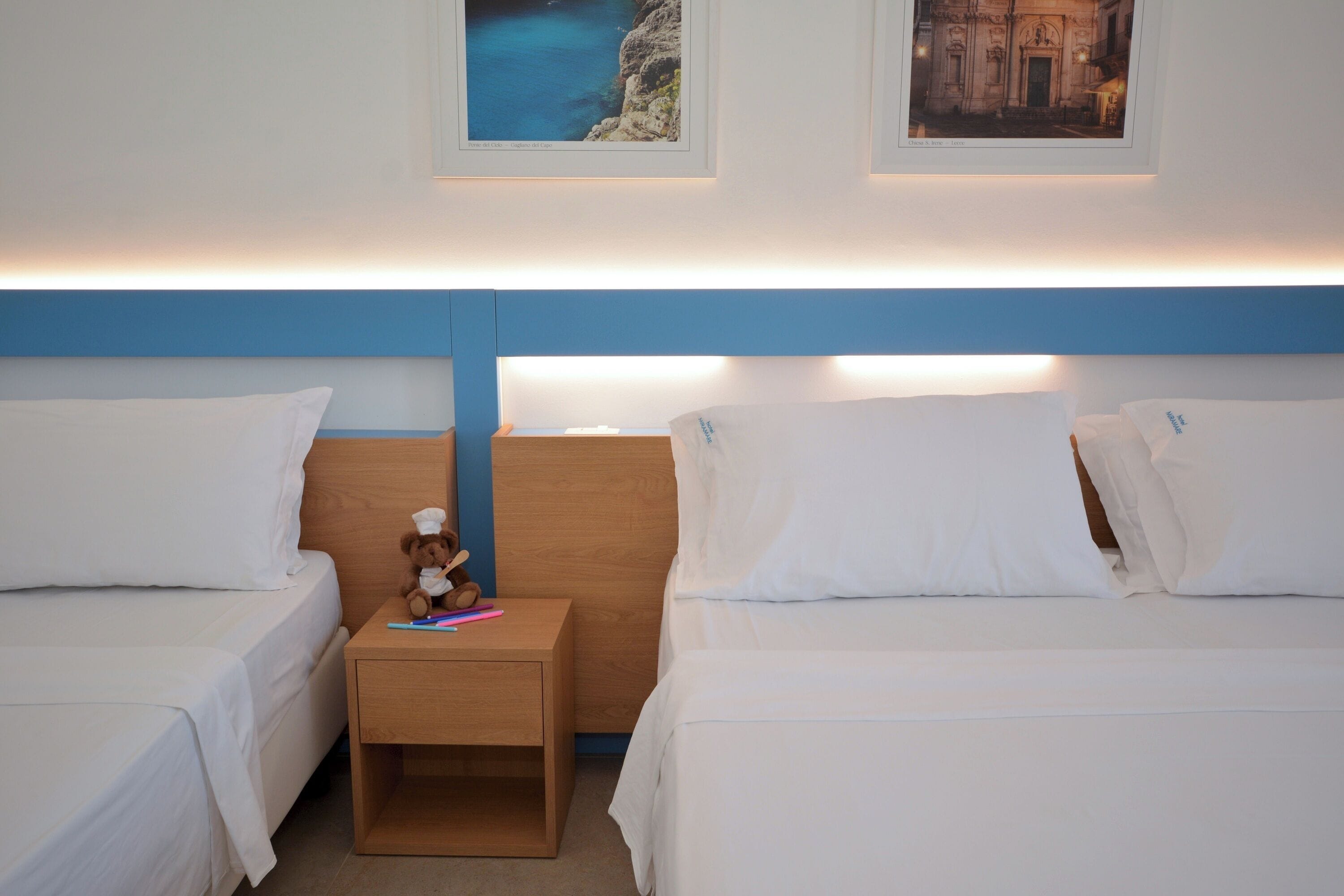 A hotel room with two beds, a nightstand, and framed pictures on the wall.