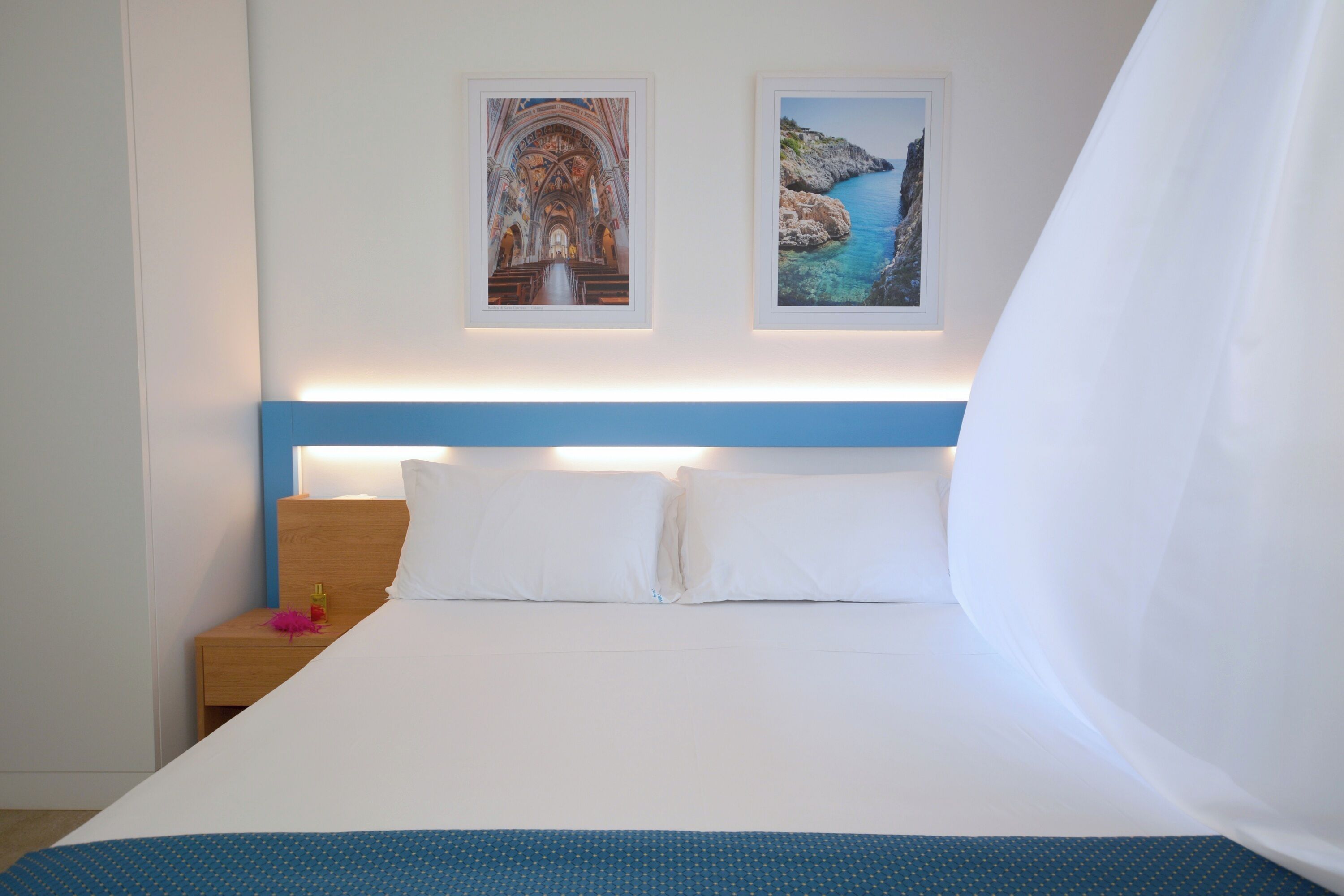 A hotel room with a bed, a nightstand, and two framed pictures on the wall.