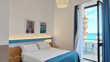 Habitación de hotel con cama, mesita de noche, lámpara colgante, balcón con vistas al mar y dos cuadros en la pared.