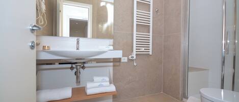 Un baño moderno con lavamanos, espejo, toallero, ducha e inodoro.