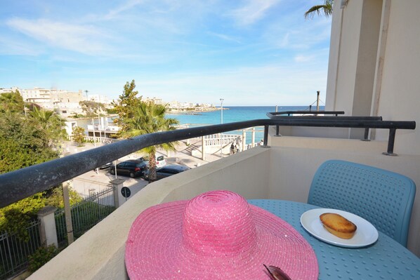 A balcony with a view of the sea, a pink hat, and a plate with a pastry.
