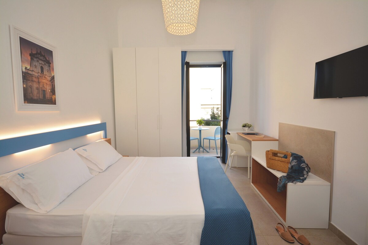 A hotel room with a bed, a desk, a chair, a TV, and a window with curtains.