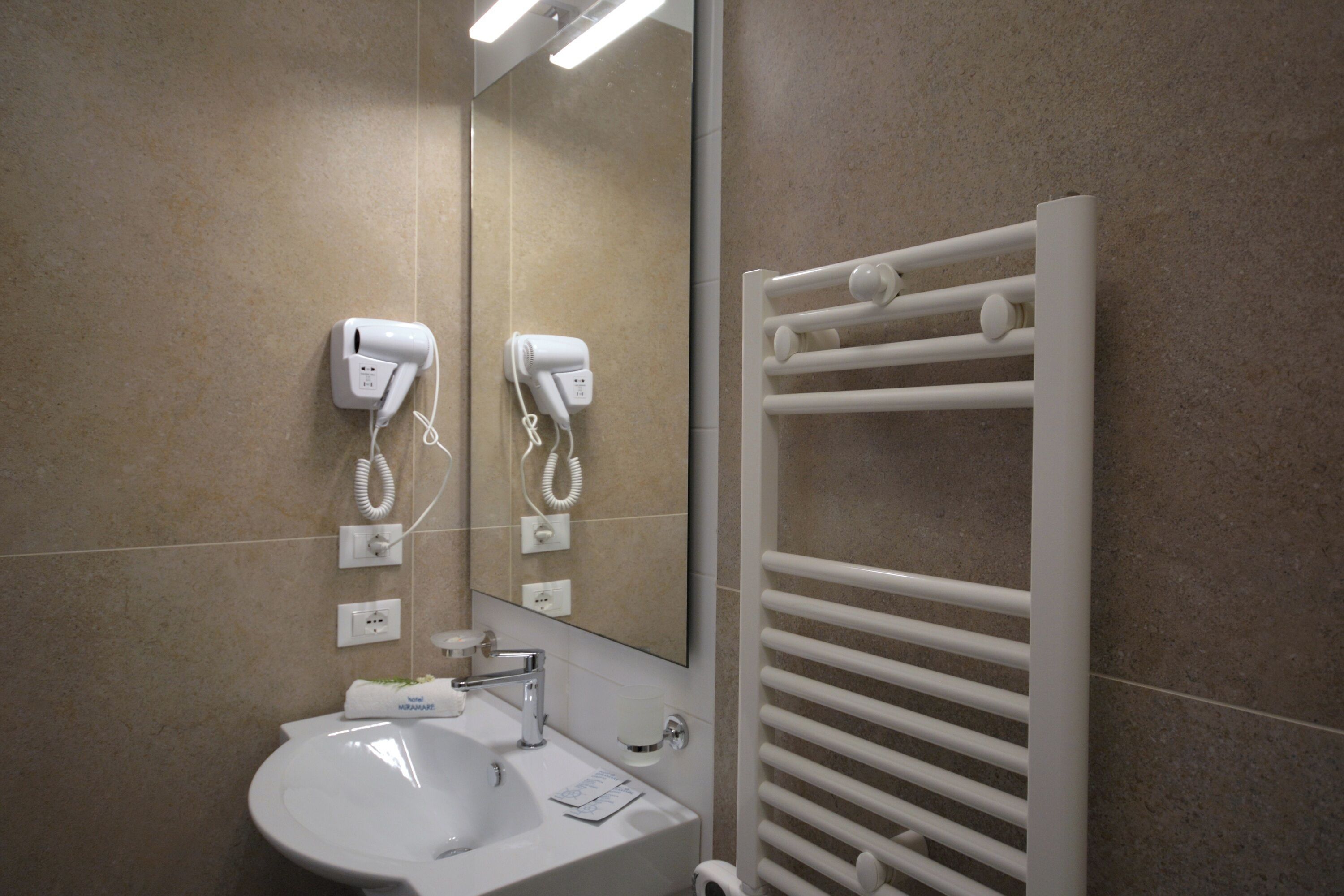 Une salle de bain équipée d’un lavabo, d’un miroir, d’un porte-serviettes et de sèche-cheveux fixés au mur.
