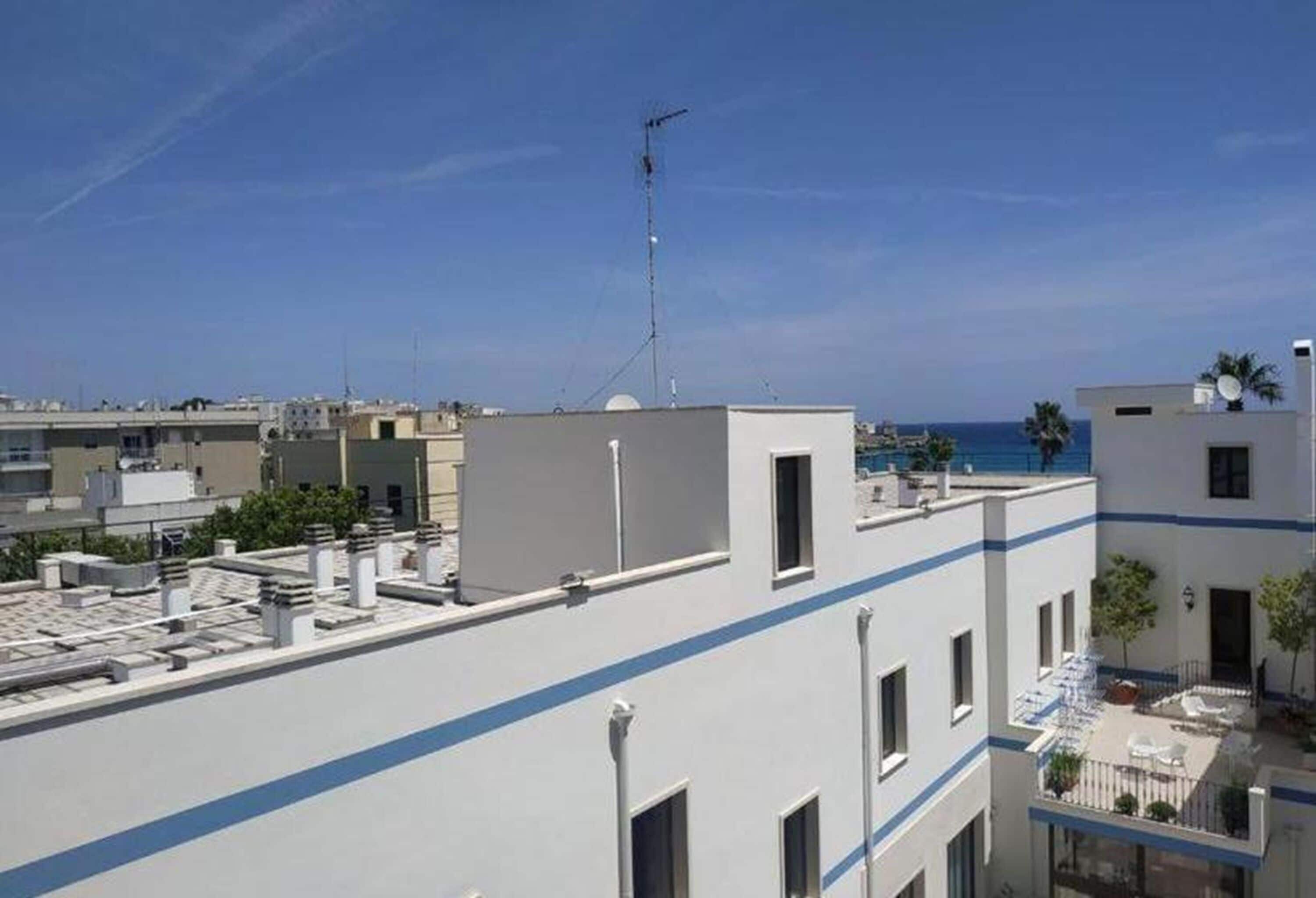 Una terraza en la azotea con vistas despejadas al mar, una antena parabólica y un edificio moderno con una franja azul.