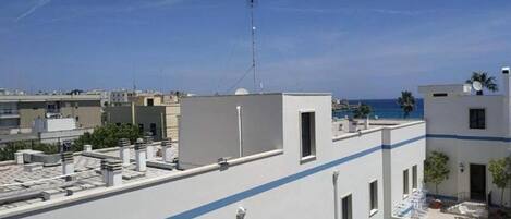 Una terraza en la azotea con vistas despejadas al mar, una antena parabólica y un edificio moderno con una franja azul.