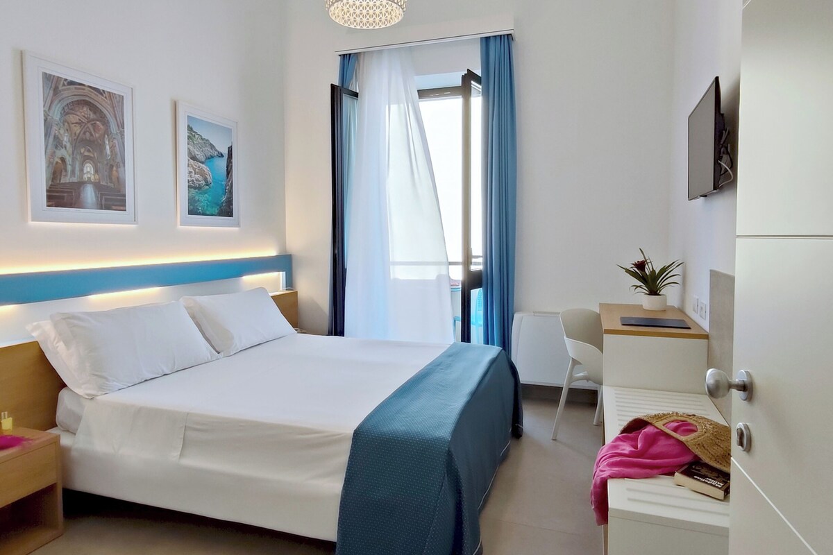A hotel room with a bed, a desk, a chair, a TV, and a window with curtains.