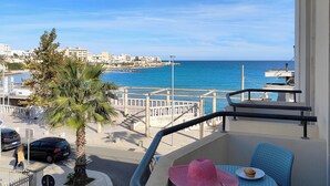 A balcony with a view of the sea, a palm tree, and a building in the background. - Hotel Miramare (Otranto)