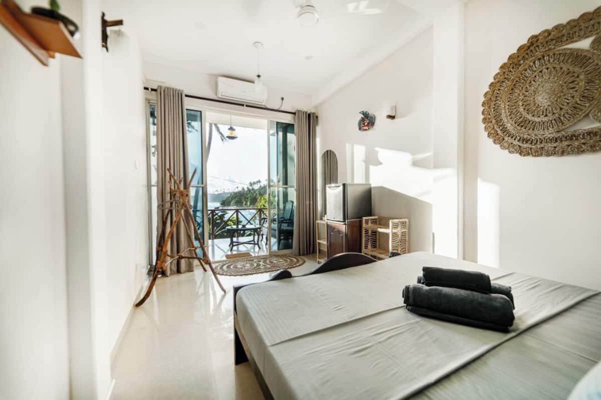A modern hotel room with a large bed, a TV, and a balcony with a view.